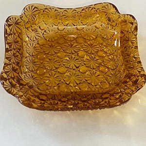Könnte beinhalten: Eine Butterschale aus bernsteinfarbenem Glas mit Deckel. Die Schale hat ein erhabenes, florales Muster.
