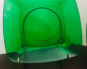 May include: A square green glass plate with a decorative, fluted design around the center. The plate is on a gold metal stand.