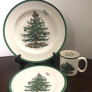 Op de afbeelding: Een set van drie kerstthema keramische schalen met een groene kerstboom met ornamenten en cadeaus. De set bevat een grote plaat, een kleinere plaat en een mok.