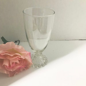 May include: A clear glass goblet with a beaded base. The goblet is empty and has a tall, slender shape.