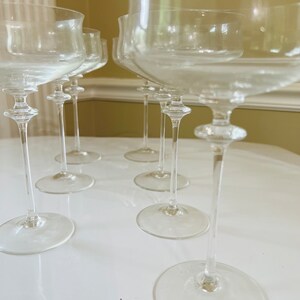 May include: A set of eight clear glass champagne flutes with a wide bowl and a long, thin stem. The flutes are arranged in a row on a white surface.