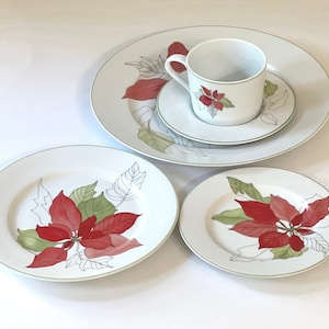 Puede incluir: Un juego de vajilla de cerámica blanca con un diseño de poinsettia verde y roja. El juego incluye una taza, un platillo, un plato para ensalada y un plato para cenar.