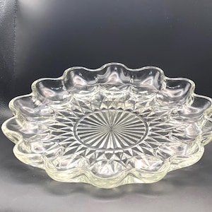 May include: Clear glass serving dish with a scalloped edge and a starburst pattern in the center. The dish has a diamond-cut design throughout and is ideal for serving appetizers or desserts. The clear glass allows the contents to be visible.