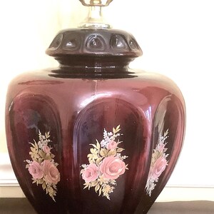 May include: A dark burgundy glass table lamp with a gold base and floral accents. The lamp has a white shade and a gold metal harp.