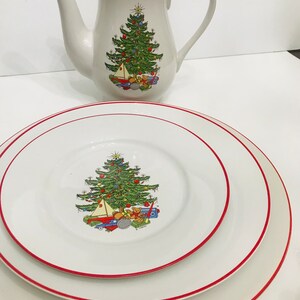 Puede incluir: Un juego de tres platos de cerámica blanca con un borde rojo. El plato central presenta un árbol de Navidad con adornos y juguetes. Los platos son parte de un juego de vajilla con temática navideña.