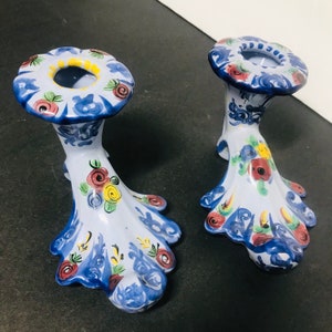 May include: A pair of blue and white ceramic candle holders with floral designs. The holders have a scalloped base and a round top with a hole for a candle.