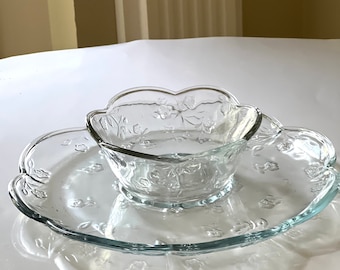 May include: A clear glass serving dish with a scalloped edge and a floral pattern. The dish is divided into two sections, one for a bowl and one for a plate.