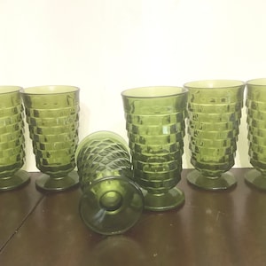 May include: Six green glass tumblers with a square patterned design. The glasses have a footed base.