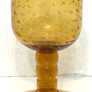 May include: A vintage amber glass goblet with a textured, bubbled surface. The goblet has a thick, rounded base and a stem with three raised rings.