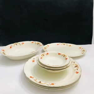 May include: A set of vintage white ceramic dinnerware with a brown and orange floral pattern. The set includes a large oval serving dish, a smaller oval serving dish, a round dinner plate, a round salad plate, and a round bowl.
