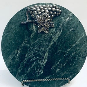 May include: A round green marble serving tray with a silver grapevine design. The tray is on a silver stand.