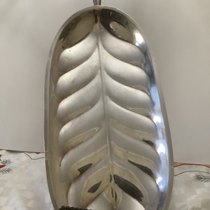 May include: Silver serving dish shaped like a leaf with a raised design. The dish has a handle on the top and is oval shaped.
