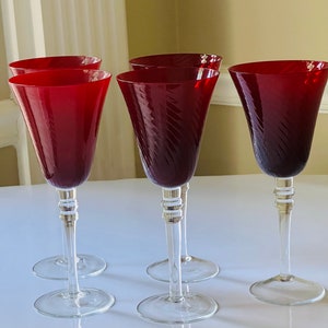 May include: Set of five red wine glasses with a swirl design. The glasses are clear with a red tint and have a tall, slender stem.