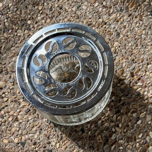 May include: Silver candle warmer with a glass base and a decorative design of leaves. The warmer has the text "Candle Warmer" printed on the side.