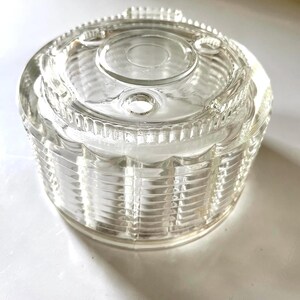 May include: Clear glass jar with a textured, ribbed design. The jar has a lid with a circular opening and three small holes.