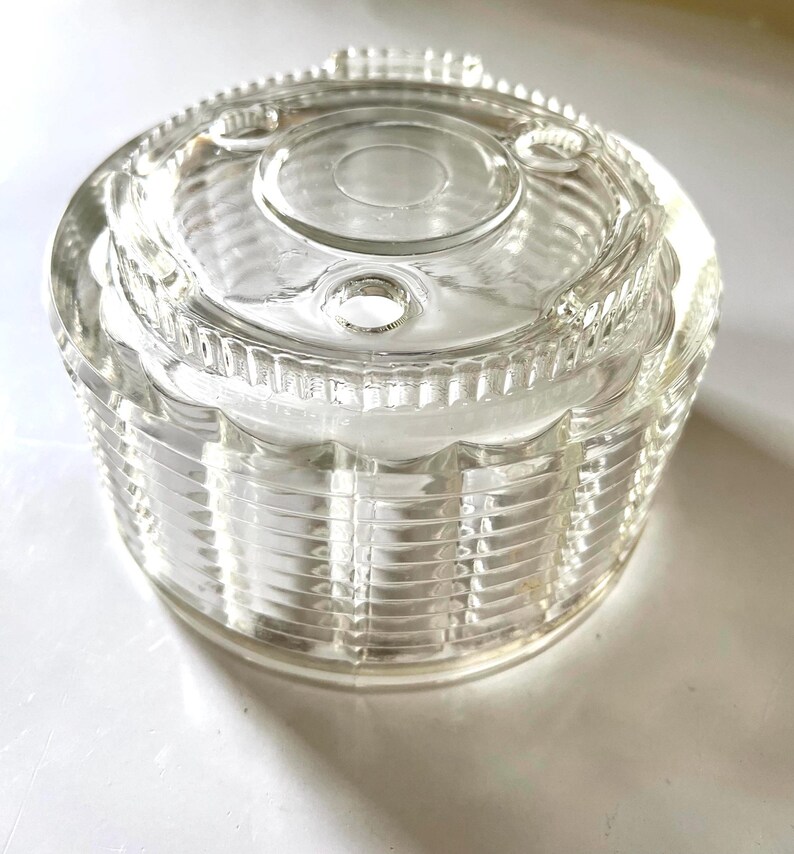 May include: Clear glass jar with a textured, ribbed design. The jar has a lid with a circular opening and three small holes.
