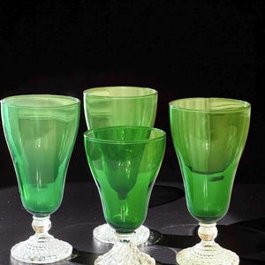 May include: Four green glass goblets with clear, textured bases and stems. The goblets have a flared shape and a vibrant green color. The bases are intricately designed, adding a touch of elegance to the glassware.