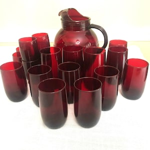 Könnte beinhalten: Ein Set mit 14 rubinroten Gläsern und einem passenden Krug. Die Gläser sind alle gleich groß und haben die gleiche Form, und der Krug hat einen Henkel.