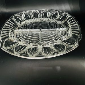 Peut inclure: Plat à servir en verre transparent avec un design divisé. Le plat de forme ovale présente une section rectangulaire centrale et un bord festonné entourant avec des compartiments individuels. Le verre a une texture nervurée.