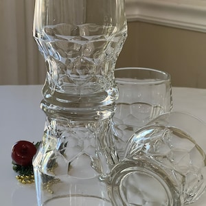 May include: Four clear glass tumblers with a textured, diamond-like pattern. The glasses are stacked on top of each other.