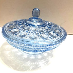 May include: A light blue glass candy dish with a lid. The dish has a decorative pattern of circles and squares. The lid has a knob on top.