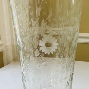 May include: A clear glass vase with an etched floral design. The vase has a wide mouth and a narrow base. The floral design features white daisies and leaves.