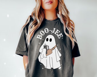 May include: A charcoal gray short-sleeve t-shirt featuring a white graphic of a ghost wearing a tan crossbody bag and holding a dark tumbler. The text BOO-JEE is printed in white above the ghost, surrounded by small star accents.