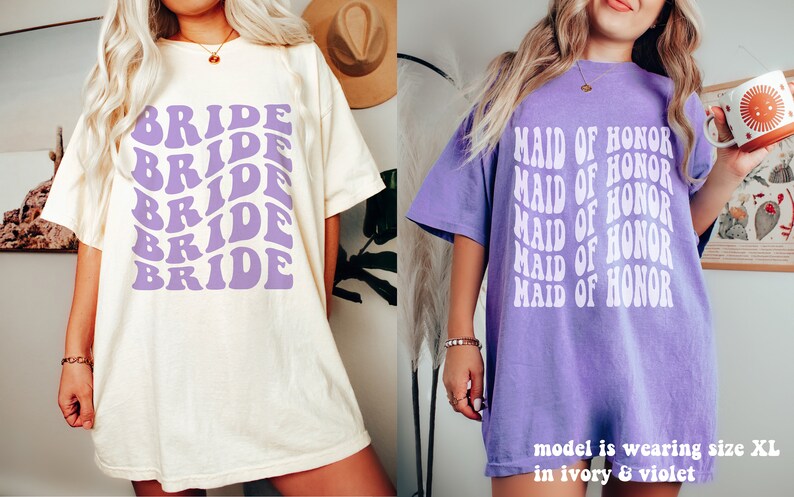 May include: Two short-sleeve t-shirts. The left shirt is ivory with the word BRIDE repeated in a wavy purple font. The right shirt is violet with the text MAID OF HONOR repeated in a wavy white font. The text states the model is wearing size XL.