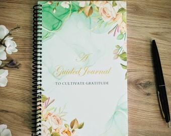 May include: A green and white spiral bound journal with a floral design and the text "A Guided Journal to Cultivate Gratitude".