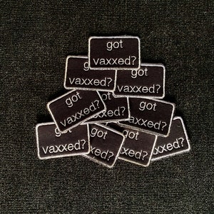 May include: A pile of black fabric patches with white text that reads "got vaxxed?"  The patches are arranged in a random pattern.