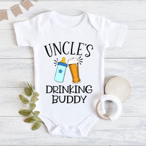 May include: White baby onesie with black text that reads "Uncle's Drinking Buddy". A baby bottle and a beer glass are pictured above the text.