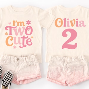 May include: Two matching cream-colored toddler t-shirts with the text "I'm Two Cute" and "Olivia 2" in pink and orange. The shirts are paired with pink shorts and black and white checkered slip-on shoes.