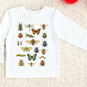 May include: White long-sleeved shirt featuring a colorful insect illustration. The design includes various bugs like beetles, butterflies, bees, and dragonflies. The shirt is made of a soft, comfortable material.