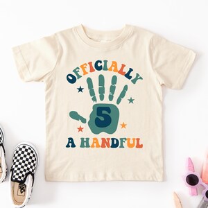 May include: A beige t-shirt with a colorful graphic that says "Officially 5 A Handful". The graphic features a handprint with the number 5 in the center.