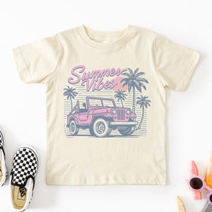 Puede incluir: Una camiseta beige claro con un jeep rosa, palmeras y el texto "Summer Vibes" en letras rosas y azules.