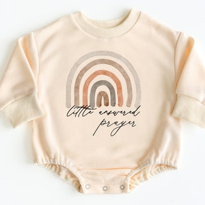 May include: A cream colored long-sleeved baby onesie with a watercolor rainbow design and the text "little answered prayer".