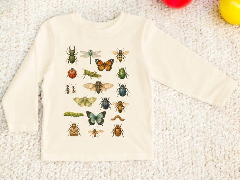 May include: Cream-colored long-sleeved shirt featuring a collection of colorful insect illustrations. The insects include a dragonfly, butterfly, ladybug, and various beetles. The shirt is made of a soft material.
