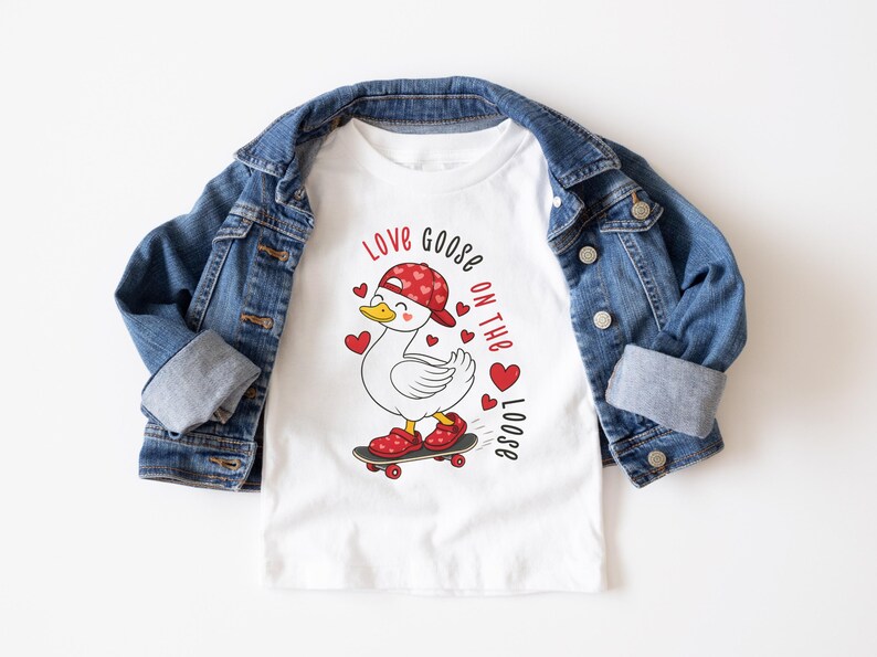 May include: White t-shirt with a cartoon goose wearing a red cap and shoes, riding a skateboard. The shirt has the text "Love Goose on the Loose" and red heart accents. A blue denim jacket is draped over the shirt.