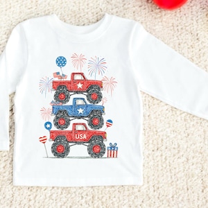 May include: White long-sleeve shirt featuring a stack of three monster trucks in red and blue, with patriotic stars and fireworks. The bottom truck has the word "USA" on it. Includes balloons and a gift.