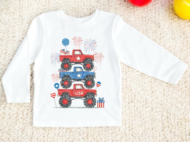 May include: White long-sleeve shirt featuring a stack of three monster trucks in red and blue, with patriotic stars and fireworks. The bottom truck has the word "USA" on it. Includes balloons and a gift.