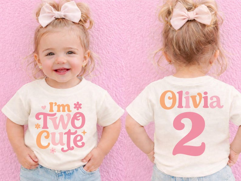 May include: A toddler wearing a cream-colored t-shirt with the text "I'm Two Cute" in pink, orange, and cream. The back of the shirt says "Olivia 2" in matching colors. The child has a pink bow in their hair.