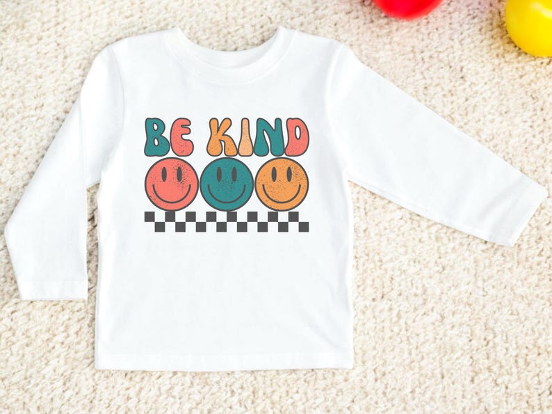 May include: White long-sleeve shirt with the text "Be Kind" in colorful letters and three smiling faces in different colors.