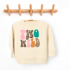 May include: A cream colored sweatshirt with the words "TWO WILD" printed on the front in colorful letters with animal print patterns.
