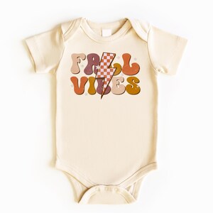 May include: A cream colored baby onesie with a retro-style graphic that says "Fall Vibes" in colorful letters with a lightning bolt in the middle.