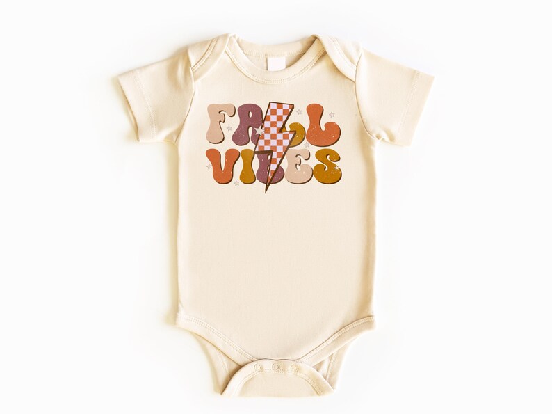 May include: A cream colored baby onesie with a retro-style graphic that says "Fall Vibes" in colorful letters with a lightning bolt in the middle.