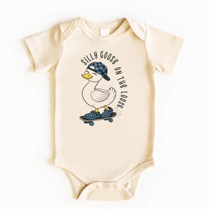 May include: Cream baby bodysuit featuring a cartoon duck in a checkered hat and shoes, skateboarding. The text "SILLY GOOSE ON THE LOOSE" is printed above the duck. The bodysuit has short sleeves and popper fastenings.