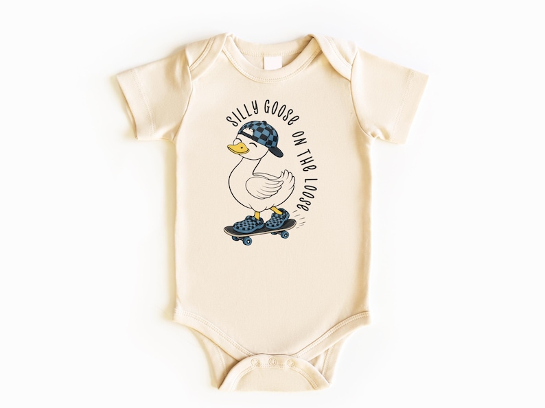 May include: Cream baby bodysuit featuring a cartoon duck in a checkered hat and shoes, skateboarding. The text "SILLY GOOSE ON THE LOOSE" is printed above the duck. The bodysuit has short sleeves and popper fastenings.
