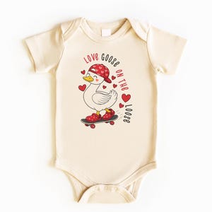 May include: Cream-colored baby onesie featuring a cartoon goose wearing a red hat and shoes, skateboarding. The text "Love Goose on the Loose" is printed in red. Red hearts are scattered around the goose.