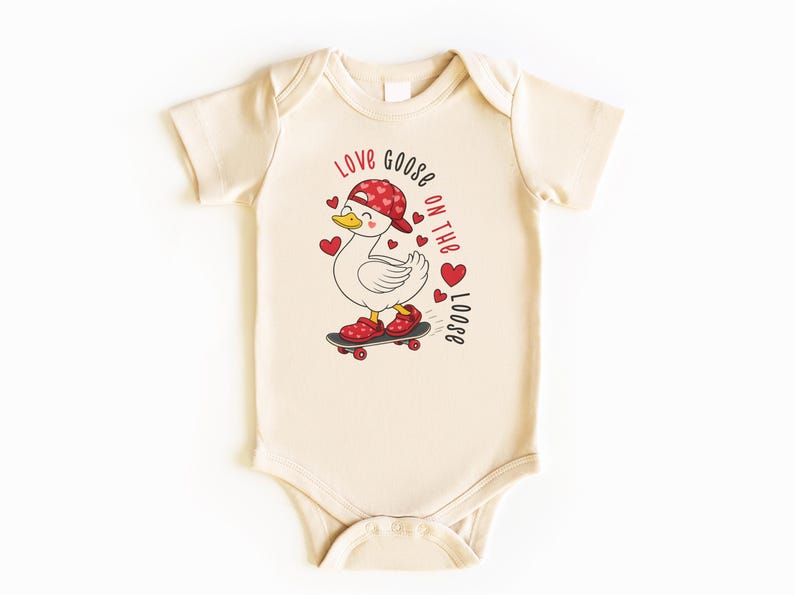 May include: Cream-colored baby onesie featuring a cartoon goose wearing a red hat and shoes, skateboarding. The text "Love Goose on the Loose" is printed in red. Red hearts are scattered around the goose.