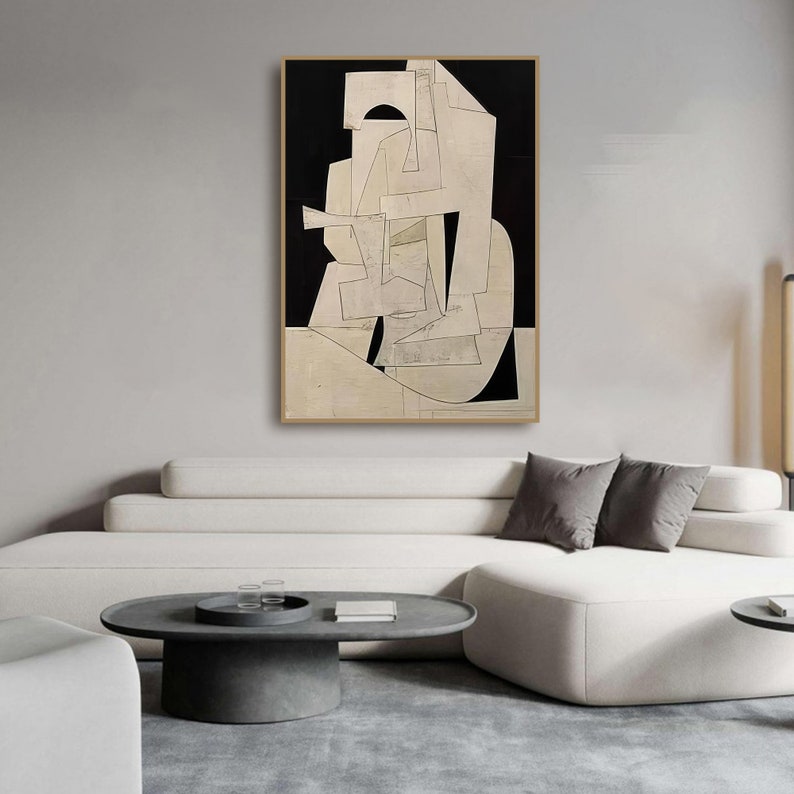 May include: Abstract art print featuring geometric shapes in black and white on a cream background. The print is framed and hanging on a wall above a white sofa.